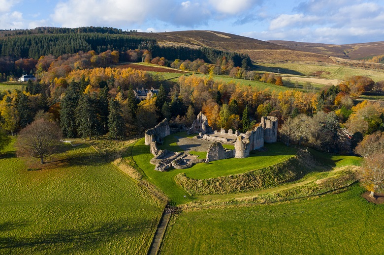 An aerial view of the extensive ruins of a castle surrounded by green trees and hills