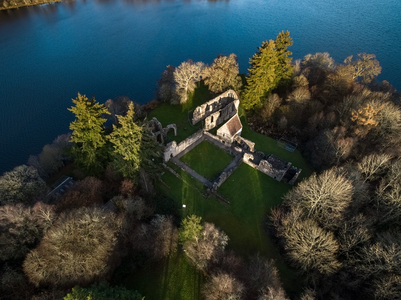 An aerial view of the ruins of a priory on a small island surrounded by winter trees