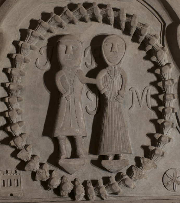 A close-up photo of a carving on a monument showing a husband and wife arm in arm