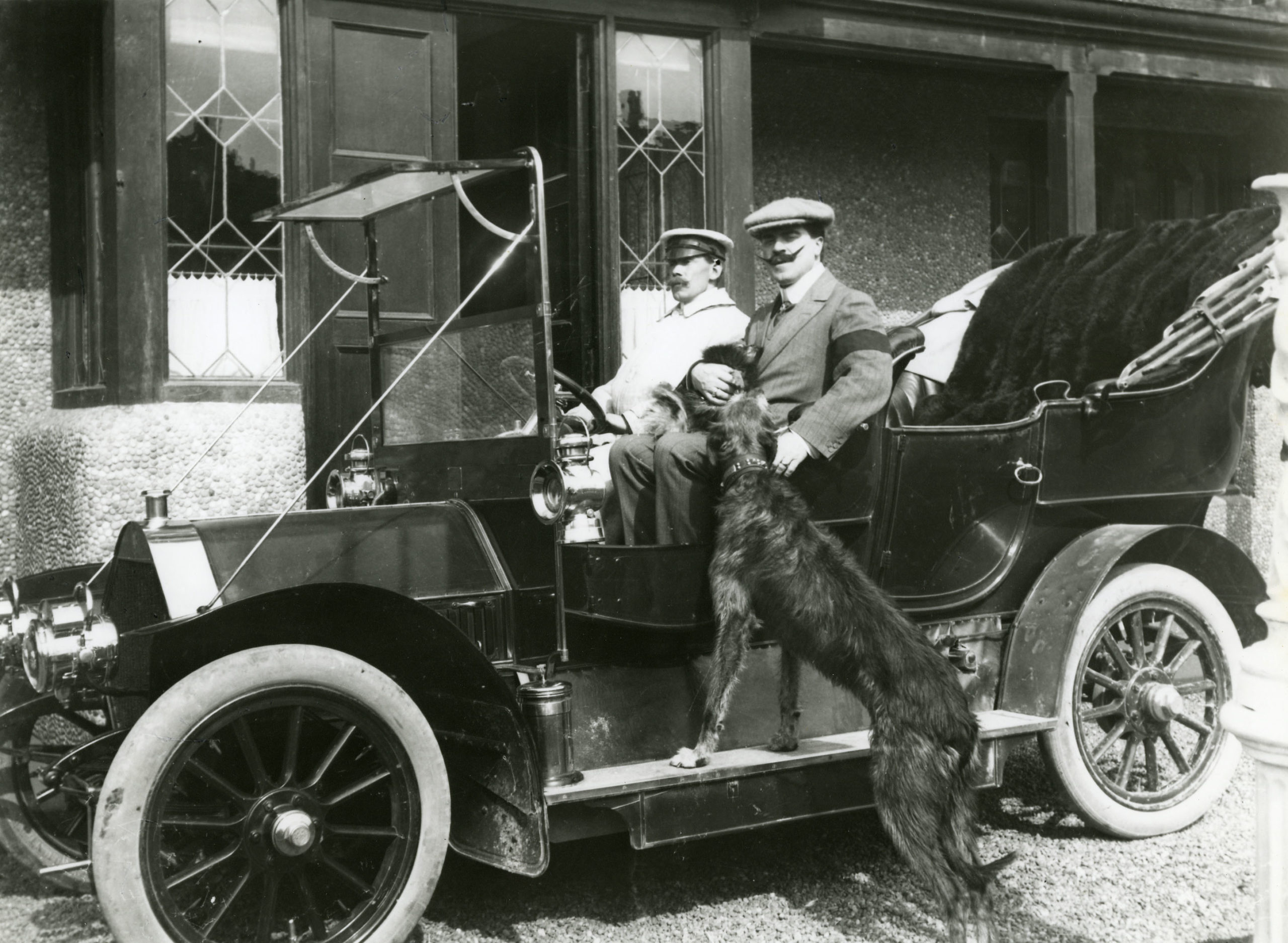 A black and white photo of Walford Bodie in a car with a dog jumping in. 