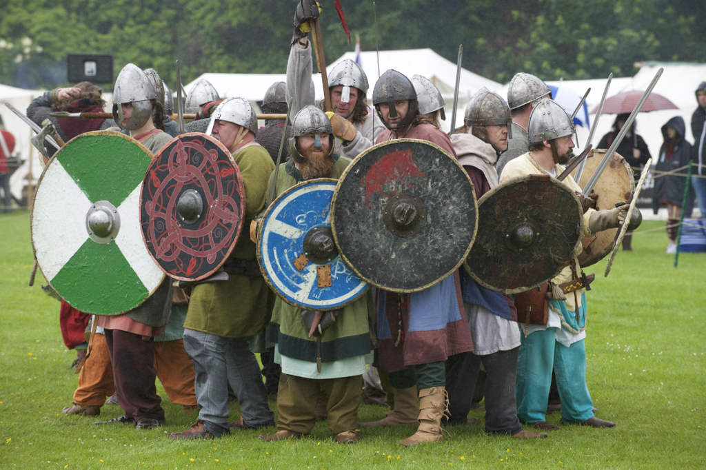 A group of people dressed in re-enactment clothing wearing helmets and carrying swords and shields