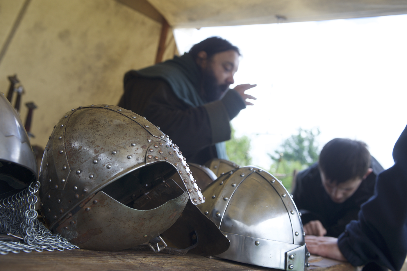 A close-up of two medieval helmets and two people in the background. 
