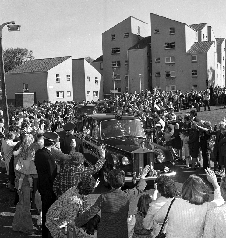 An archive photo of crowds waving as a number of cars, one carrying The Queen, arrives in an Edinburgh suburb