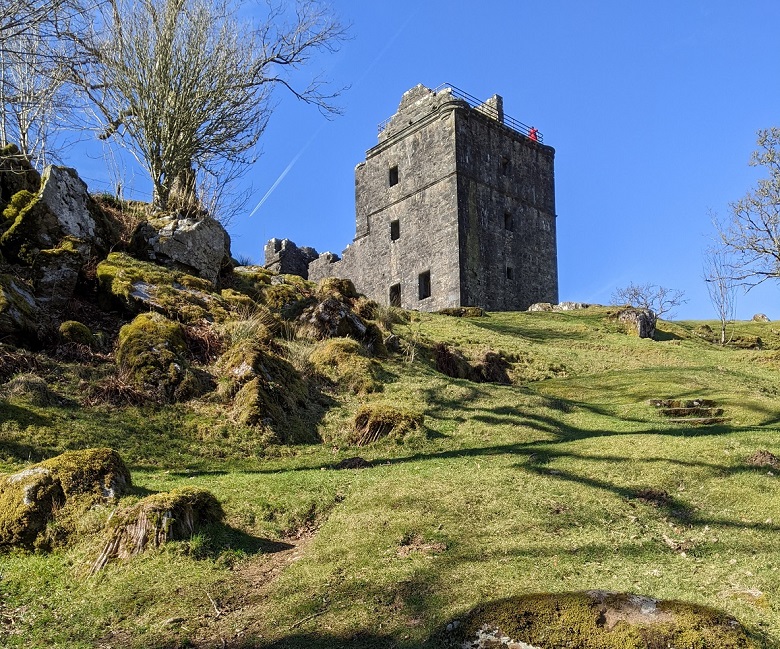 A rectangular, small stone castle on top of a grass hill