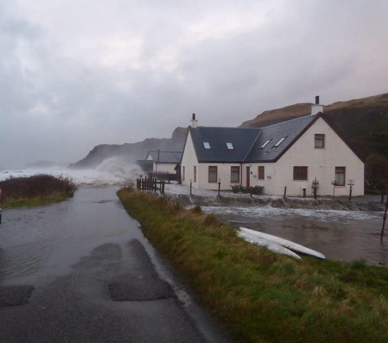 Water from the sea battering against the shore across a road, beside a house
