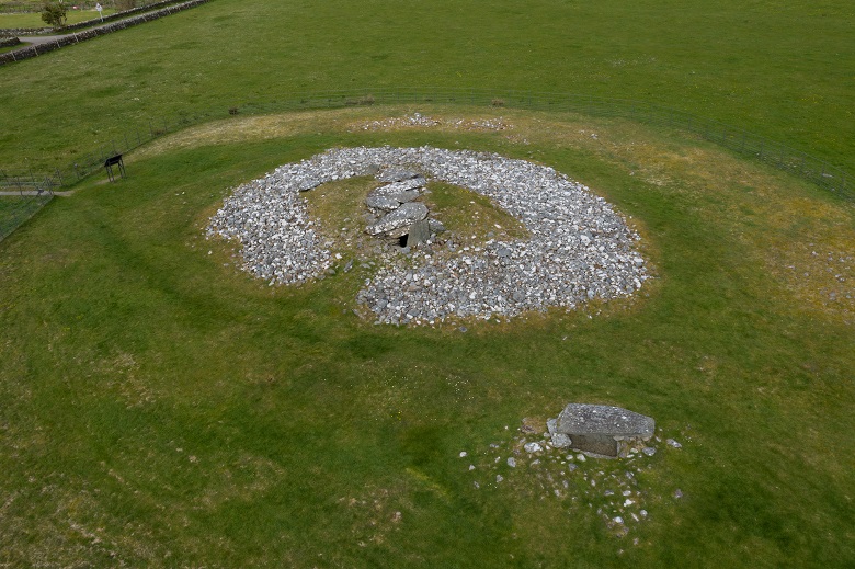 A view from above of a circular historic cairn in a field. The cairn is made up of many small stones