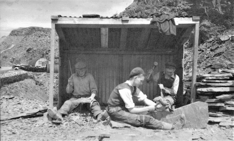Three people sitting in a shelter on a slate quarry, splitting slates
