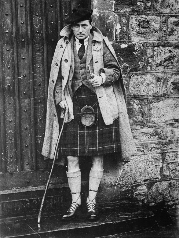 Compton MacKenzie photographed wearing a kilt and holding a pipe and walking stick