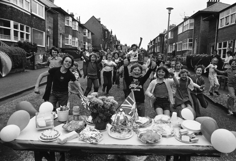 Children pose excitedly for the camera in front of a table of food at at a street party 