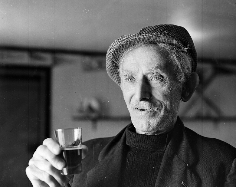 An archive photo of an elderly man raising a glass of whisky