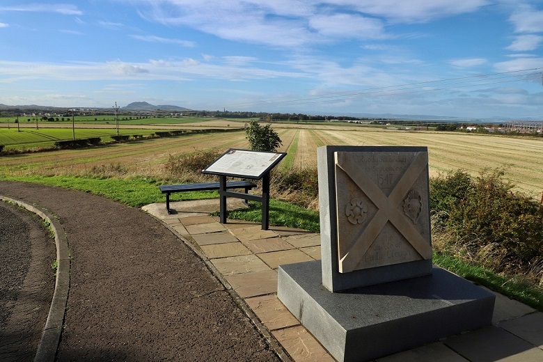 A memorial and a information panel at the site of a battlefield. now an agricultural field 