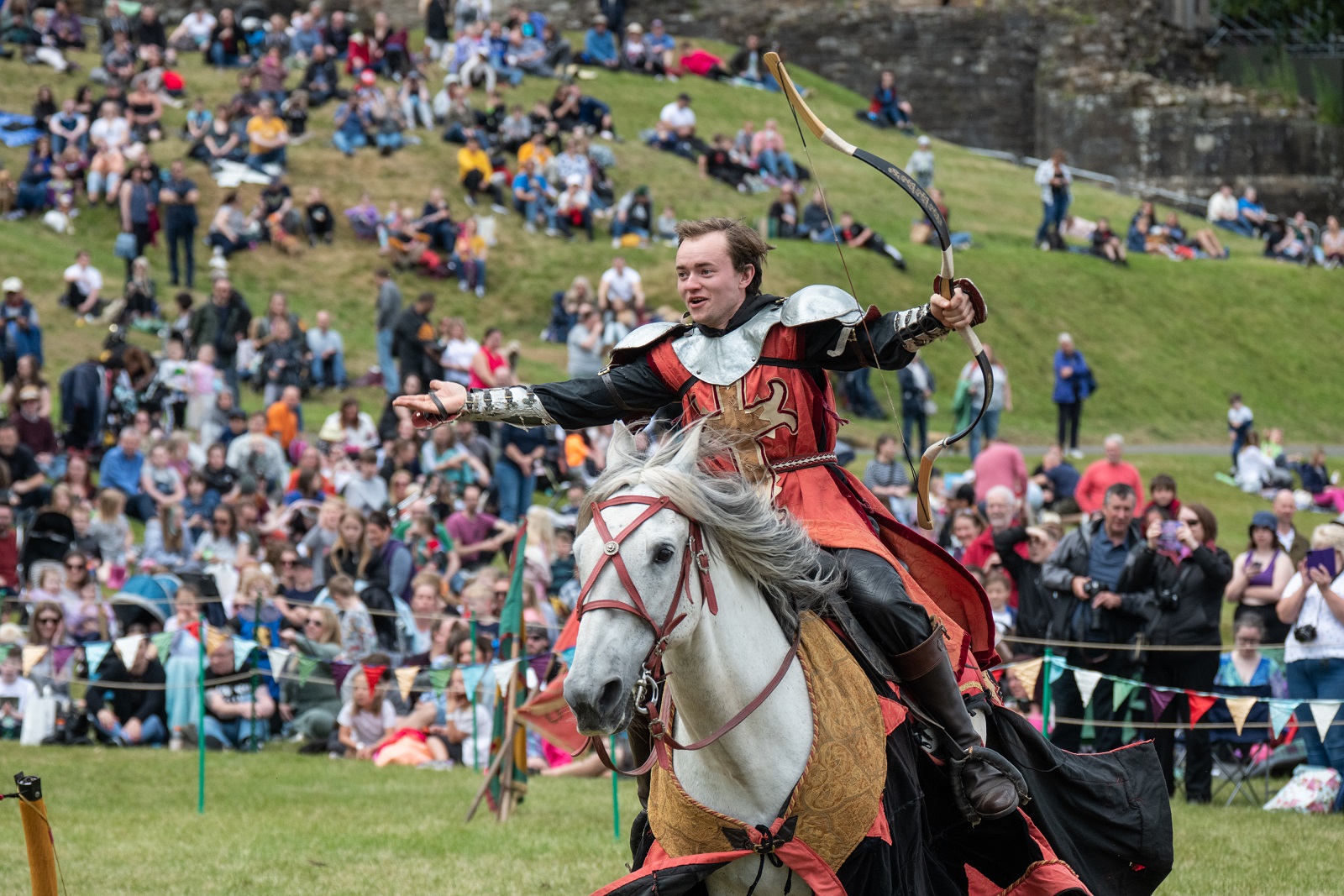 Knight on a horse riding. He's carrying a bow and arrow and looks at the audience triumphantly.