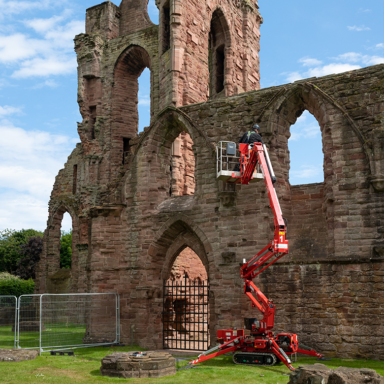 a cherry picker carries people up a wall to inspect masonry at an abbey