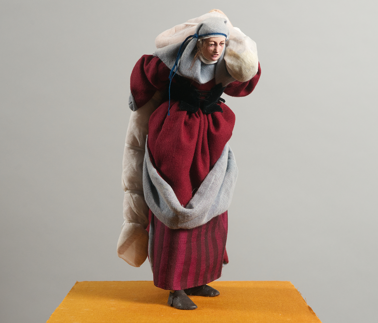 A model of a lady in a red dress carrying a body wrapped in a white cloth on her back