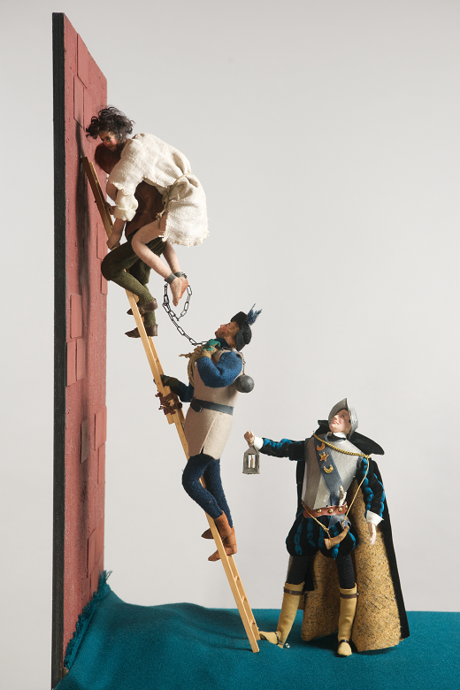 A model of a prisoner in chains being helped down a ladder by another man, while a third stands at the foot of the ladder with a lantern