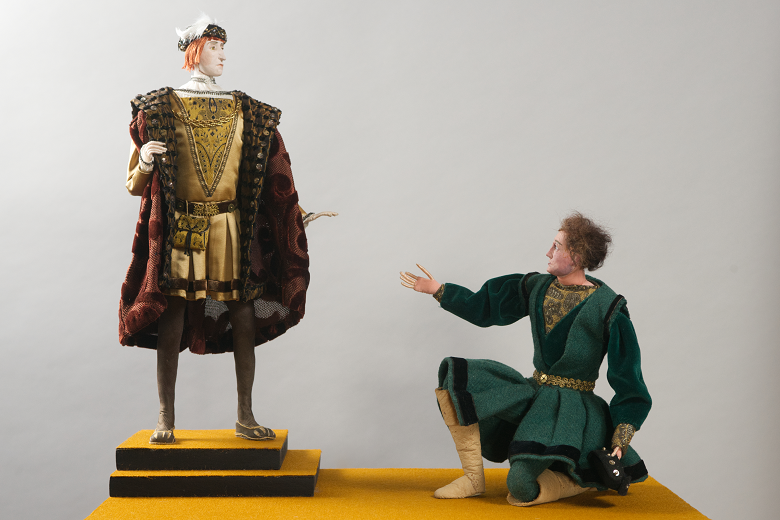 Two models side by side. A king in regal clothing stands over a man in a green tunic who kneels at the king's feet. 