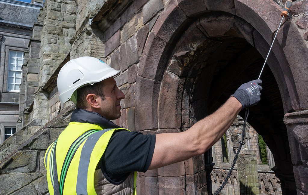 man in PPE inspects a stone arch