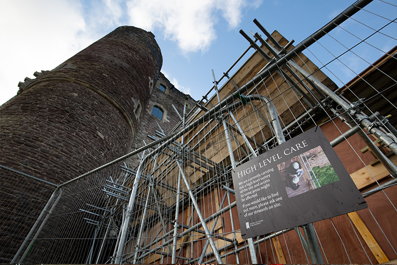 Doune Castle with fencing and a sign in the foreground. The sign reads "high level care"
