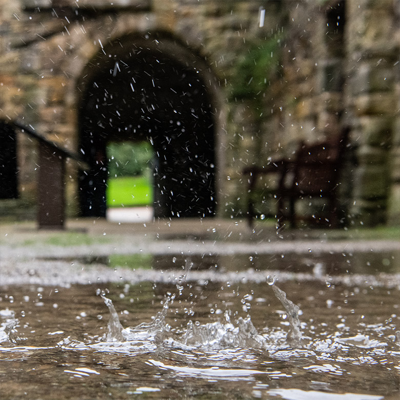 a large, deep puddle with rain splashing into it with inchcolm abbey behind