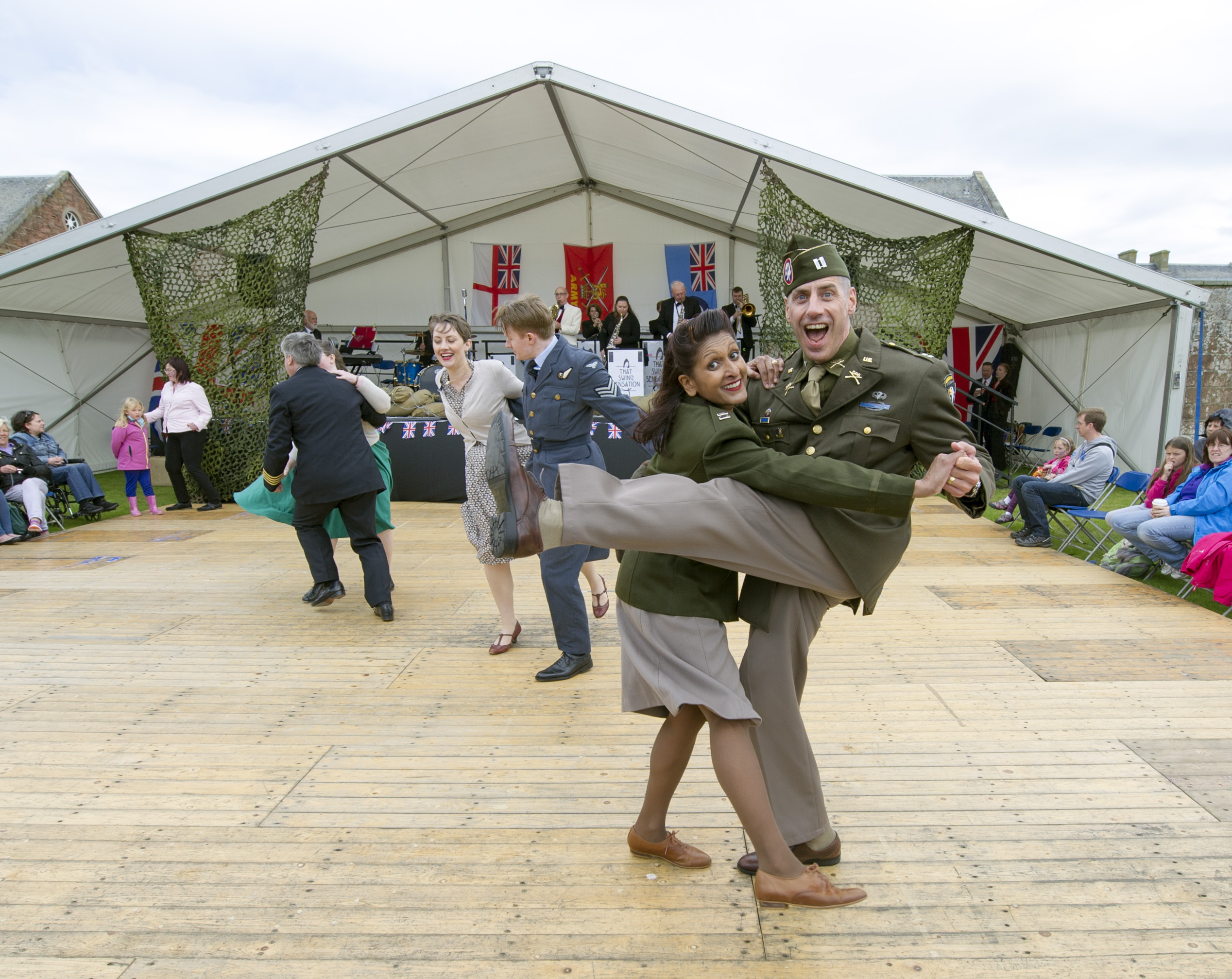 An image of two people dressed in re-enactment army clothes dancing in front of a large open tent for Celebration of the Centuries