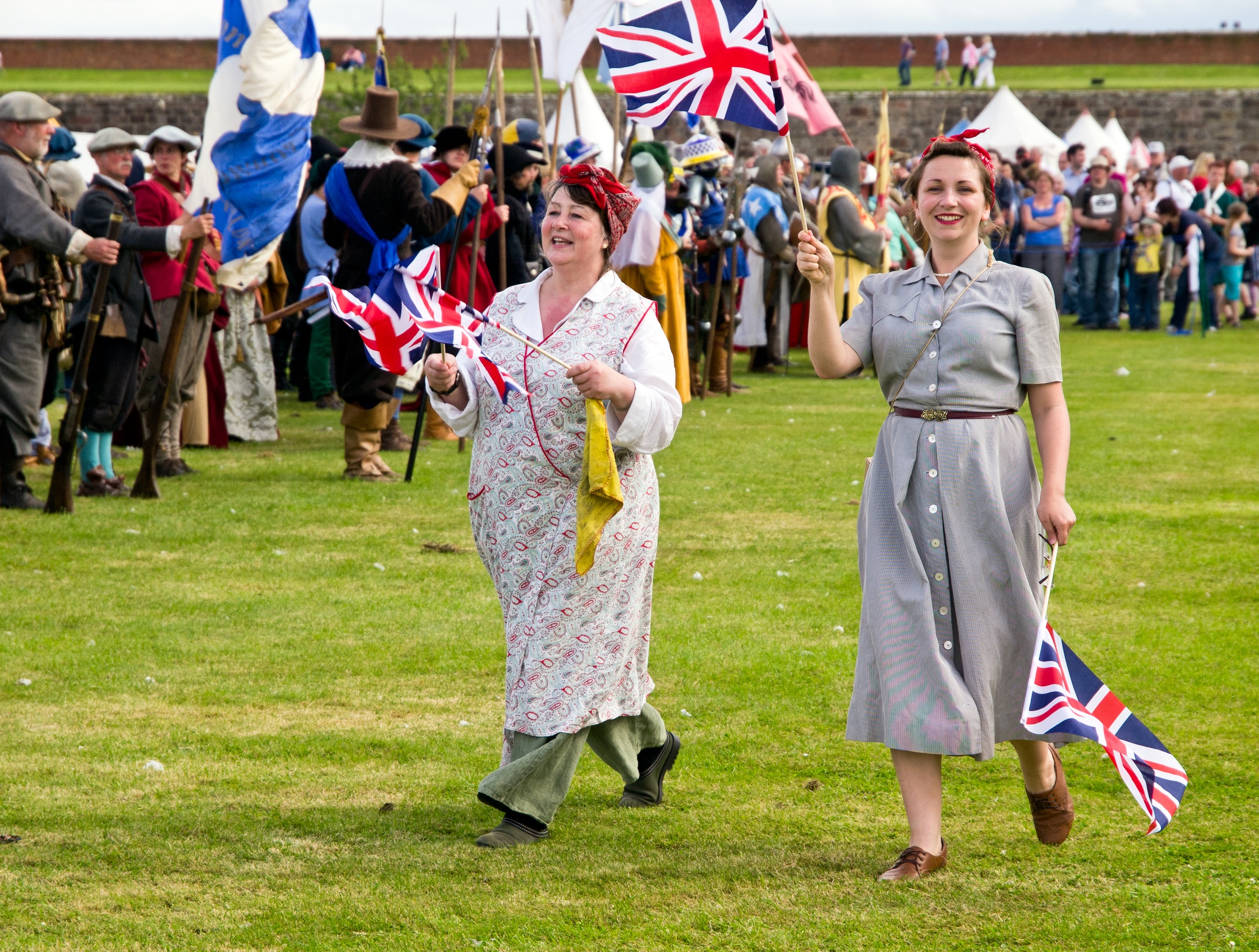 Two people dressed in re-enactment vintage, war-time clothes carrying Union Jacks for Celebration of the Centuries