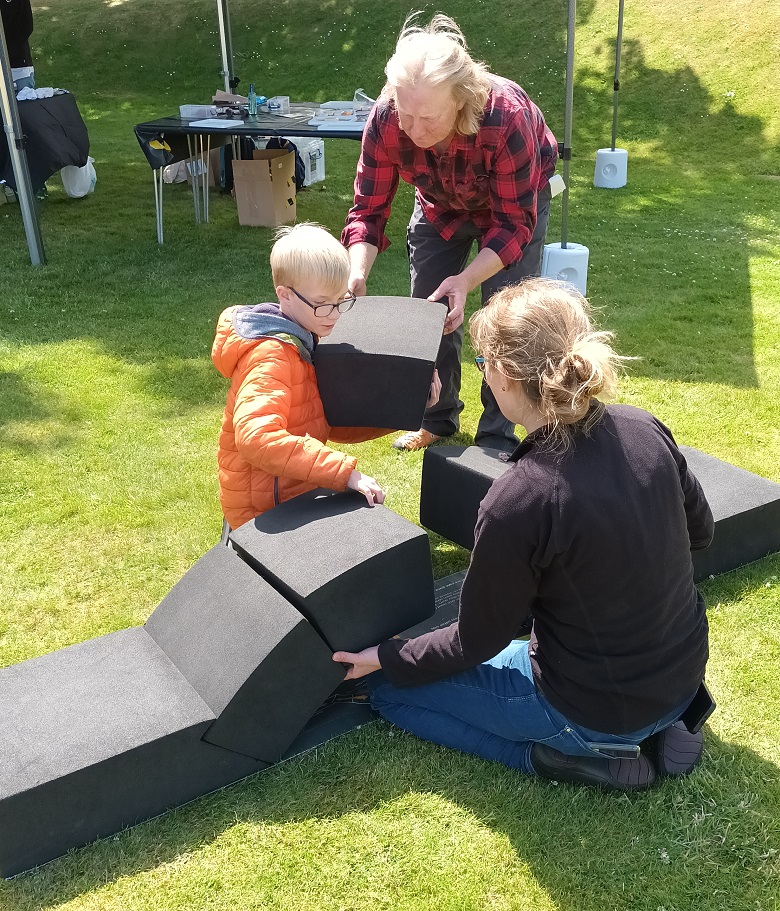A child, a parent and a member of HES staff play with large foam bricks