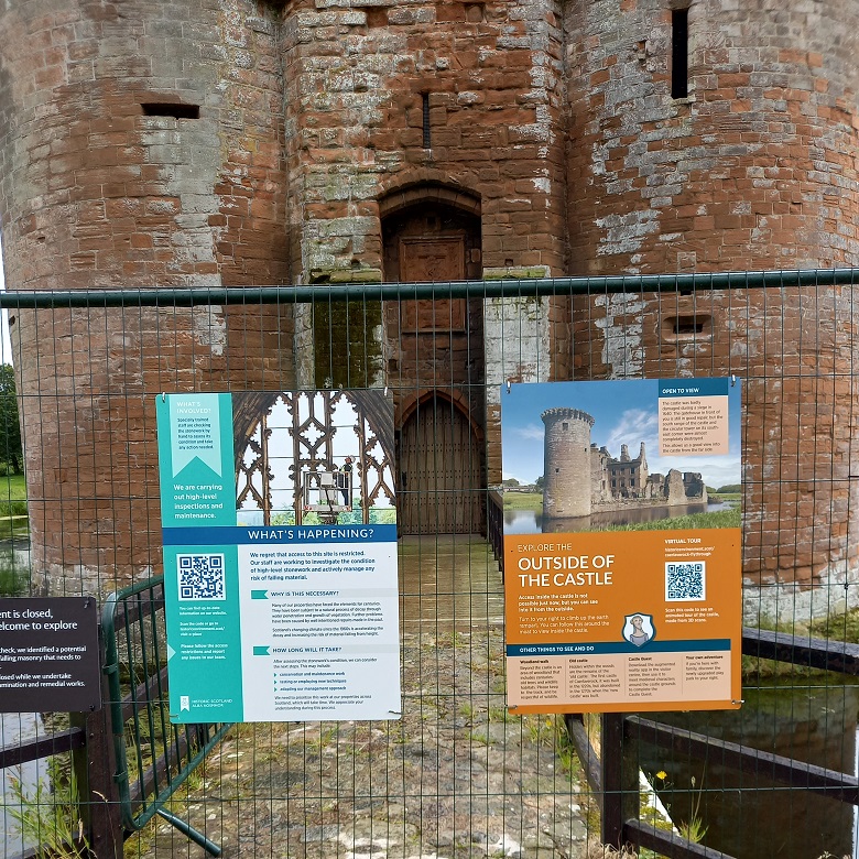 Two panels attached to a fence at Caerlaverock Castle. The panel on the left features a photo of inspections work at Melorse and a QR code to more information.