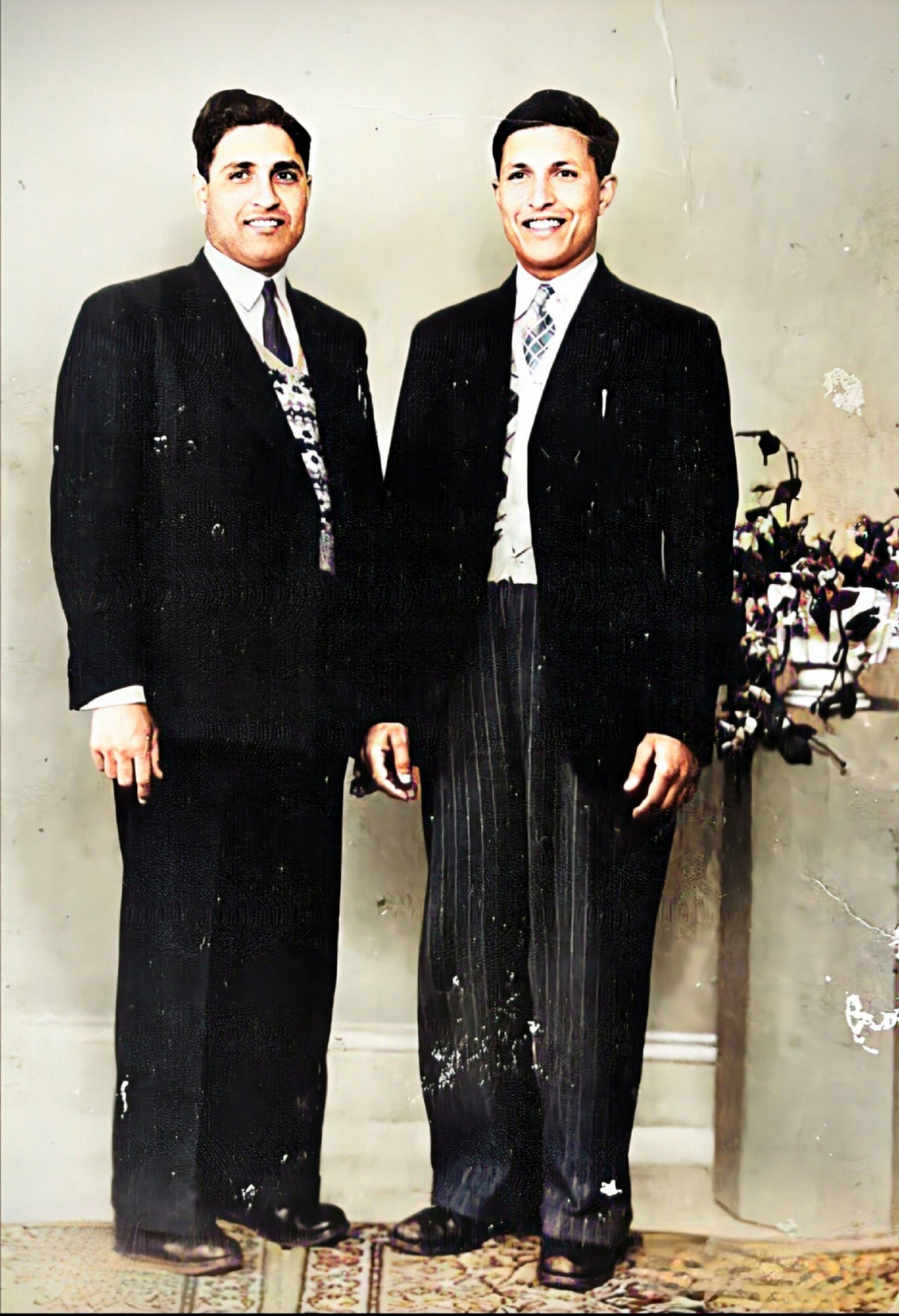 Two people standing next to each other for a photo. They are wearing suits. 