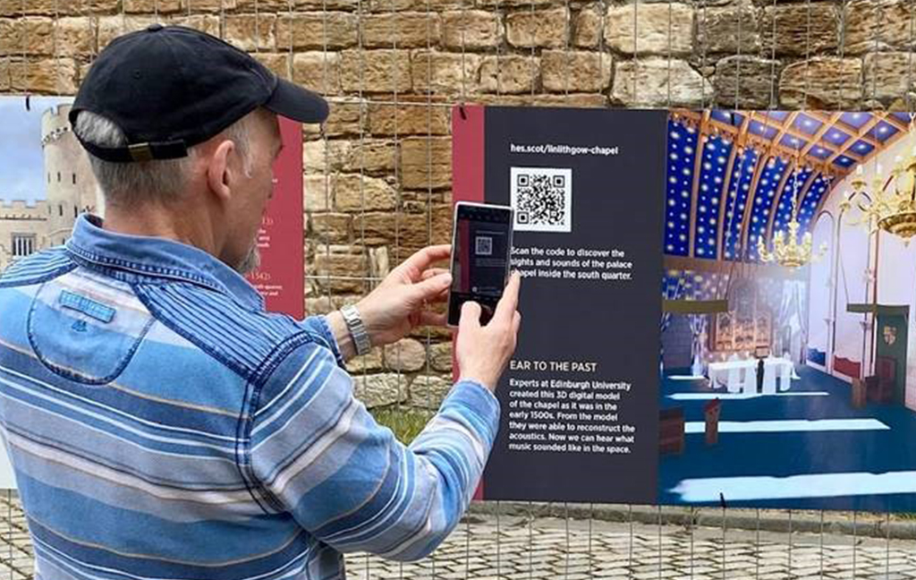 Visitor scanning the QR code on the new interpretation graphics added to the heras fencing around Linlithgow Palace, which in place due to High Level Masonry inspecitons.