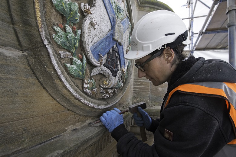 A person wearing PPE carries out conservation on a carved panel of the mercat cross.