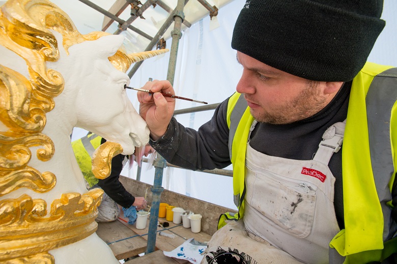 Man in PPE paints the eye detail on a carved unicorn