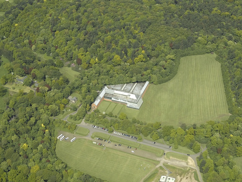 An aerial view of the Burrell Museum building hugging the tree line in a country park