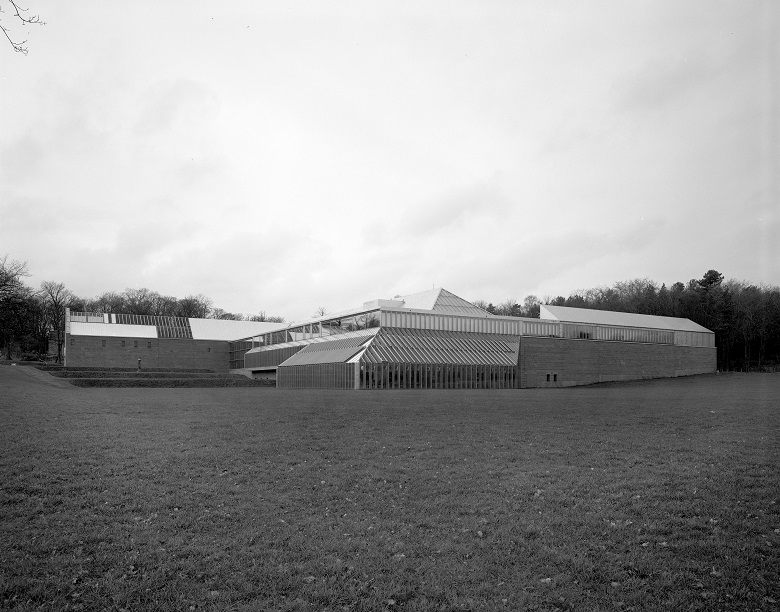 A black and white photo of a purpose built modern museum building surrounded by parkland 