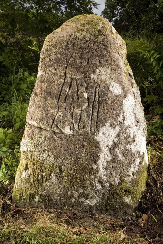 an upright stone carved with the figure of a person with a staff, club or sword.