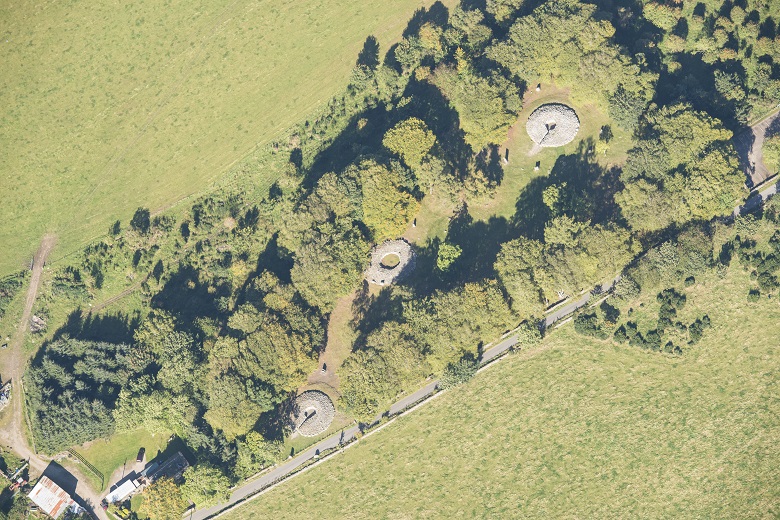 Aerial view of Clava Cairns which shows three stone "doughnuts" (the burial cairns) set amongst trees.