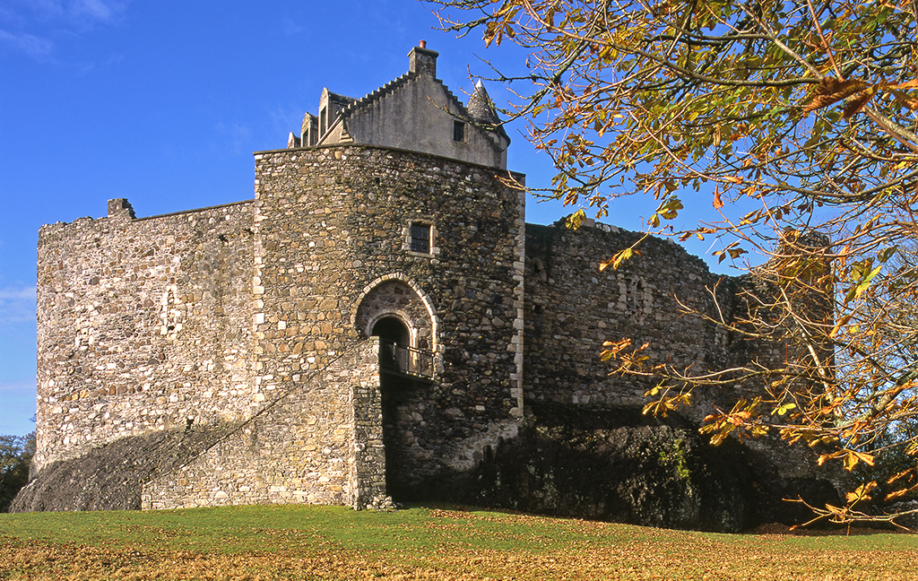 Dunstaffnage Castle on a lovely autumnal day. The sky is blue and there are leaves on the lawn.