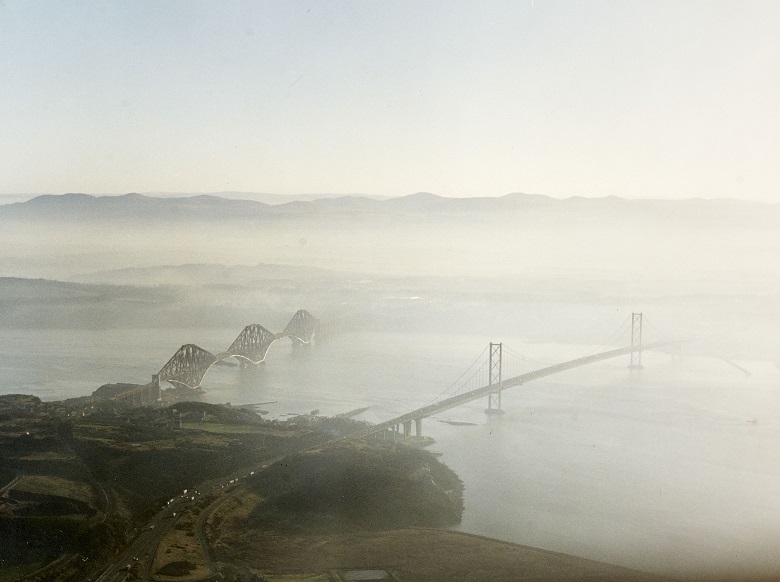 An aerial photo of low cloud gathered around a large suspension bridge 
