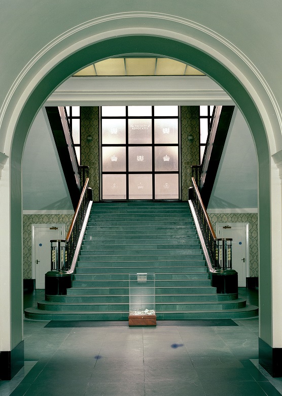 An archway leading to a large green or turquoise staircase backed by a window with a stained glass emblem in each frame