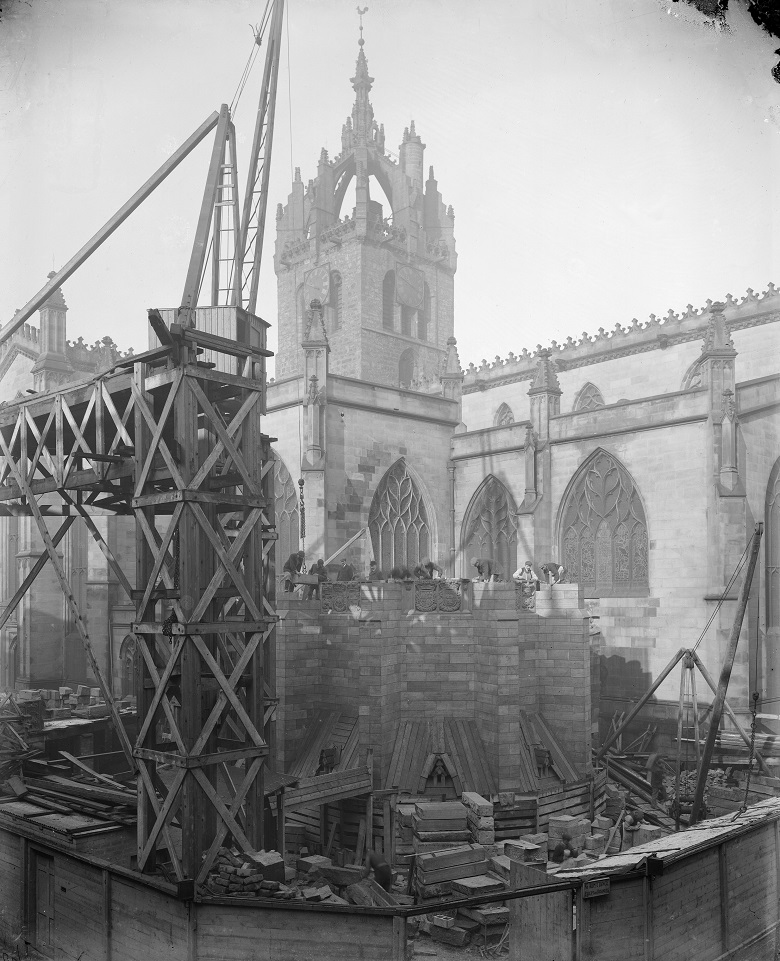 Construction work taking place outside St Giles Cathedral in 1911. Scaffolding and cranes are made of wood. Construction workers wear clothing of the day, including flat caps, tweed jackets and aprons. 