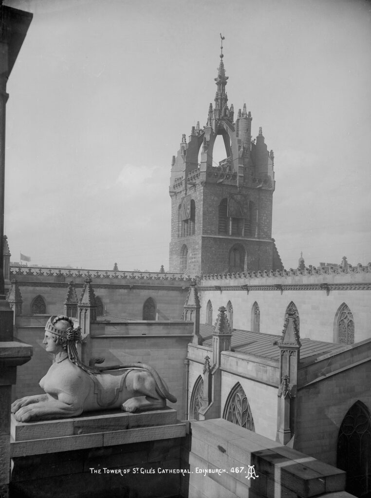 An elevated view of the crown-shaped spire of St Giles' viewed from the Supreme Courts, with a carved sphynx in the foreground.