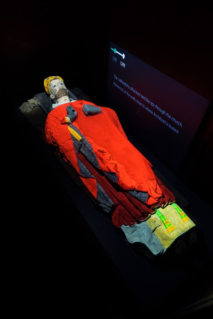 a carved stone effigy bathed in coloured light depicting how it may have looked originally when painted.