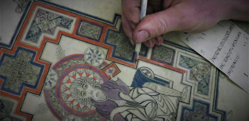 A close-up photo of an artist using a stylus to add colour to a reproduction of the Book of Kells