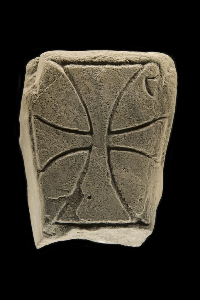 View of a small cubed stone carved with a simple cross.