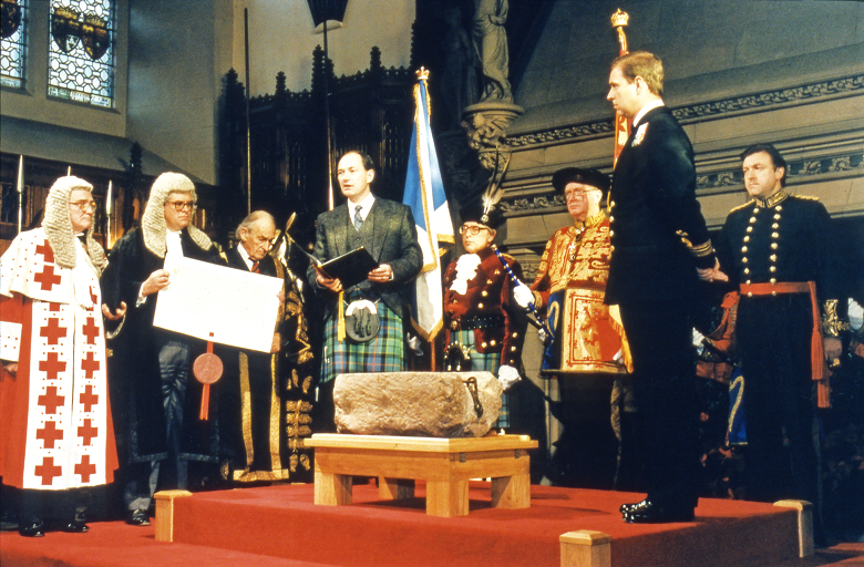 The Stone of Destiny on a plinth on a stage in front of dignitaries in ceremonial outfits 