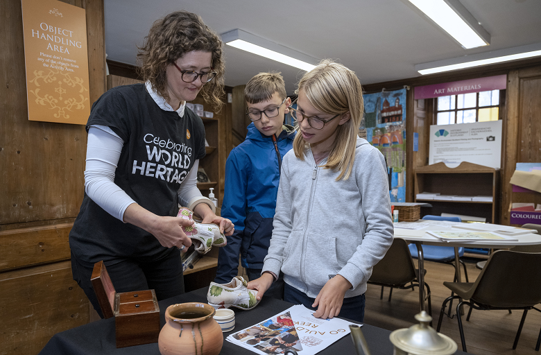 A member of Historic Environment Scotland stafff points out details on a replica of a historic shoe to two young learners