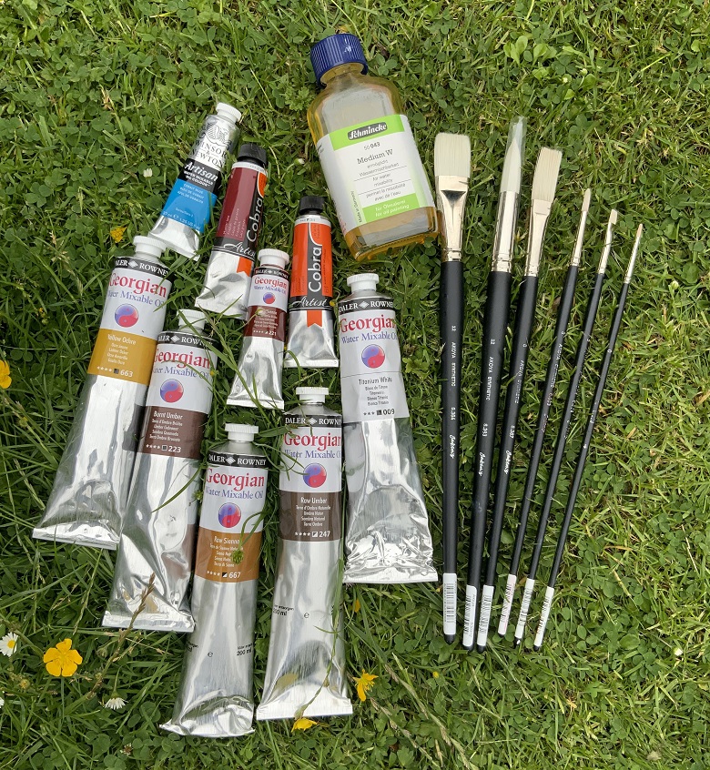 Tubes of paint and paintbrushes laid on a lawn.