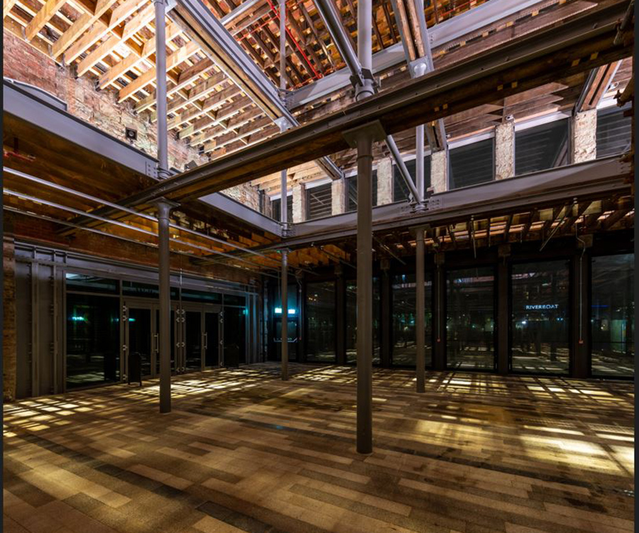 Interior of building with open steel pillars and beams. The floor wood with light reflecting on it from the ceiling.