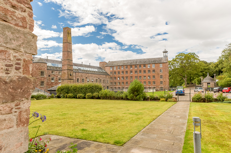 A tall chimney besides a large mill building