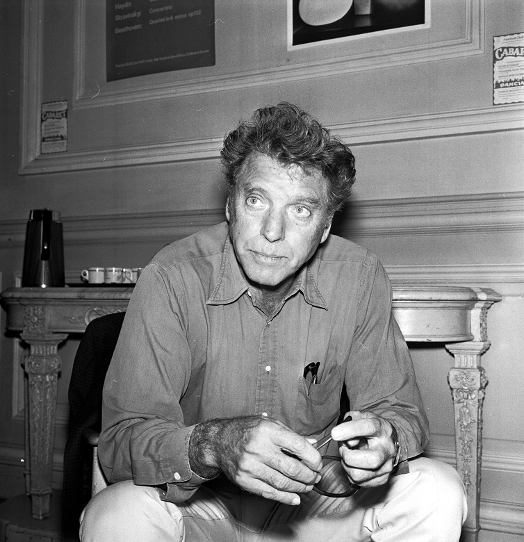Burt Lancaster sitting on a chair holding a pair of glasses