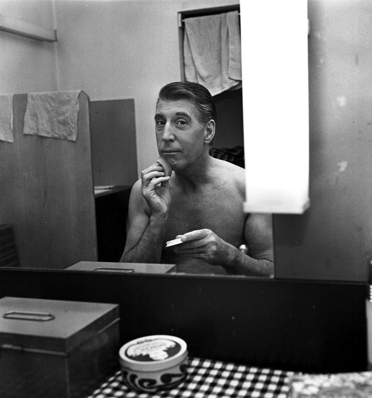 An actor applying make up in a cramped theatre dressing room